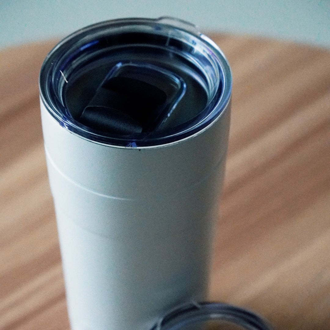 White tumbler with a clear lid on a wooden surface